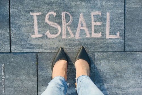 View from above, female feet with text Israel written on grey sidewalk.