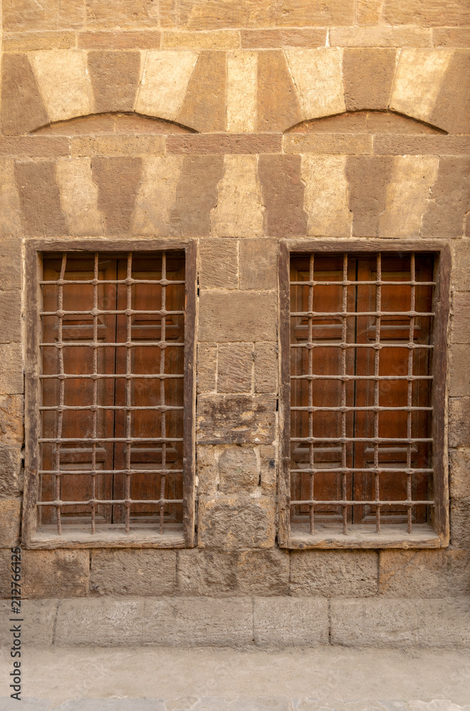 Obraz premium Two similar adjacent wooden closed windows with iron grid over decorated stone bricks wall, Medieval Cairo, Egypt