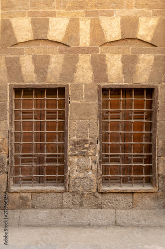 Two similar adjacent wooden closed windows with iron grid over decorated stone bricks wall, Medieval Cairo, Egypt © Khaled El-Adawi
