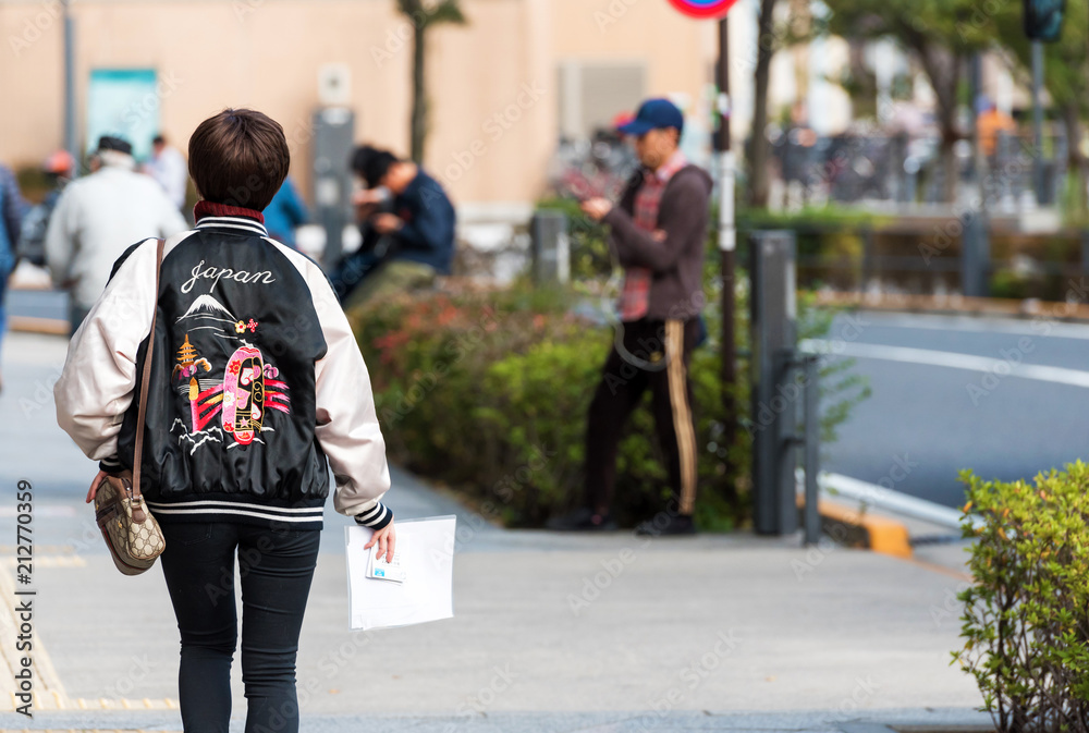 TOKYO, JAPAN - NOVEMBER 7, 2017: A woman in a jacket with the inscription Japan on a city street. Copy space for text. TOKYO, JAPAN - NOVEMBER 7, 2017: A woman in a jacket with the inscription Japan on a city street. Copy space for text.