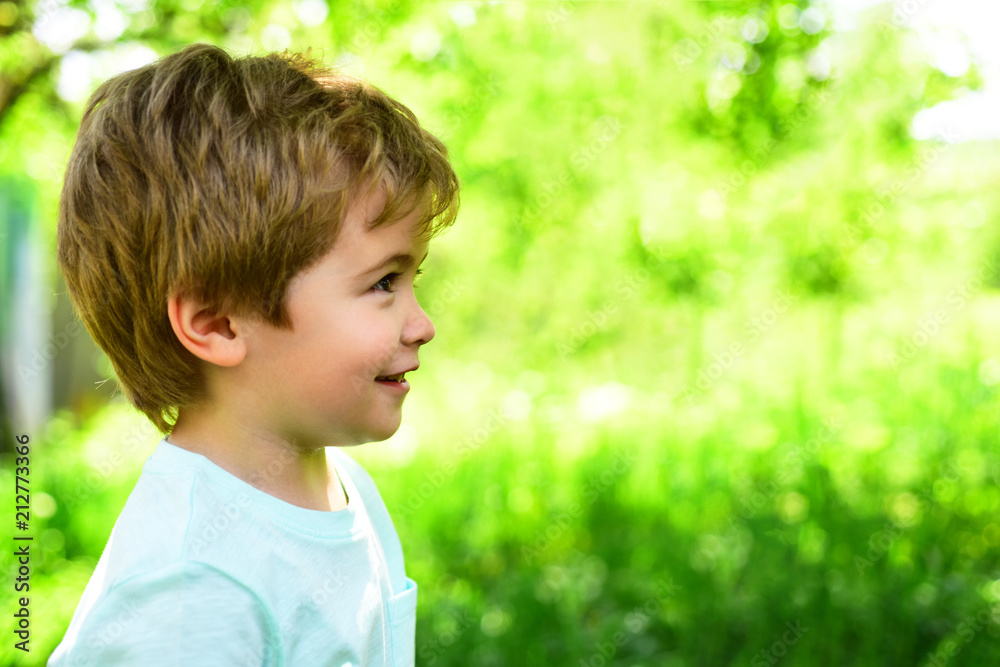 Cute smiling boy looks at something. Family walk in garden during warm sunny day. Family holidays with children in countryside. Green natural background during summer Cute smiling boy looks at something. Family walk in garden during warm sunny day. Family holidays with children in countryside. Green natural background during summer