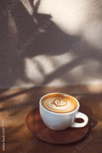 Cup of cappuccino with beautiful heart shape latte art. Tropical and hipster vibes. Plants shadows. Sul lights and shadows.