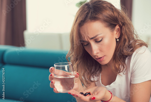 stressed depressed attractive young woman with painkiller pills and glass of water