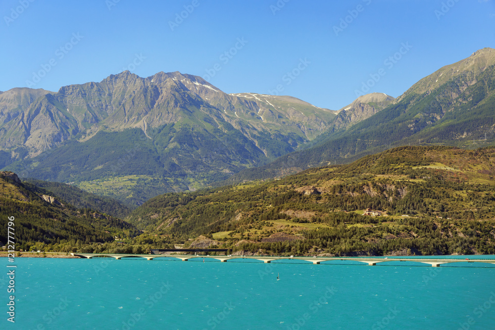 .Car bridge over the Serre Poncón artificial lake in the French Alps. Lake water is used for irrigation of agricultural fields. This is a popular tourist destination.
