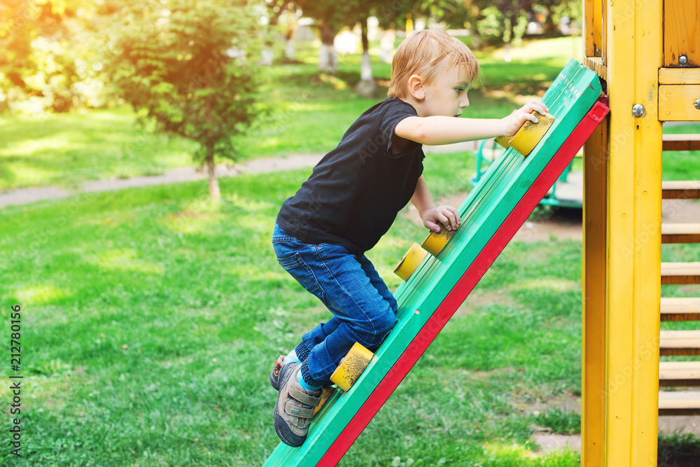Happy kid climbing on outdoor playground. Little blond boy having fun outdoors. Summer, spring and autumn leisure for active kids. Child climbs confidently up on kids playground. Summer holidays. Happy kid climbing on outdoor playground. Little blond boy having fun outdoors. Summer, spring and autumn leisure for active kids. Child climbs confidently up on kids playground. Summer holidays.