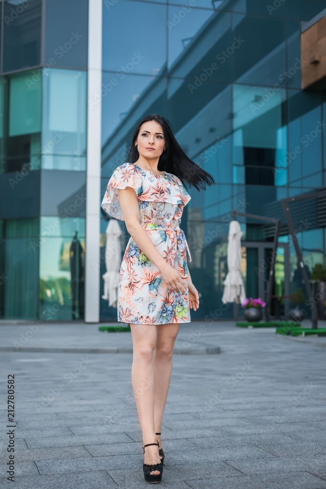 Naklejka premium portrait of young successful girl with long brunette hair, wearing white dress with flower on the urban background