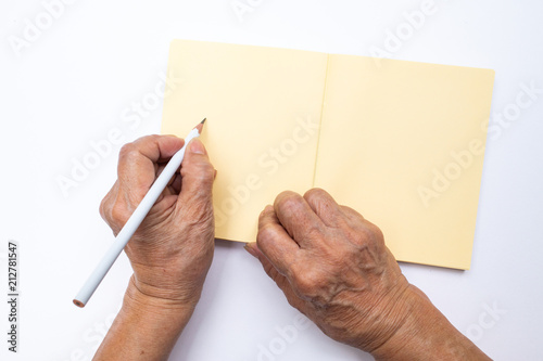 Senior woman's left hand with white pencil writing on notebook isolated on white background, Stationery concept