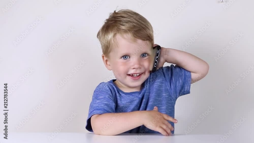 Little kid boy with mobile phone in hands, looking in it and talking on white background Little kid boy with mobile phone in hands, looking in it and talking on white background