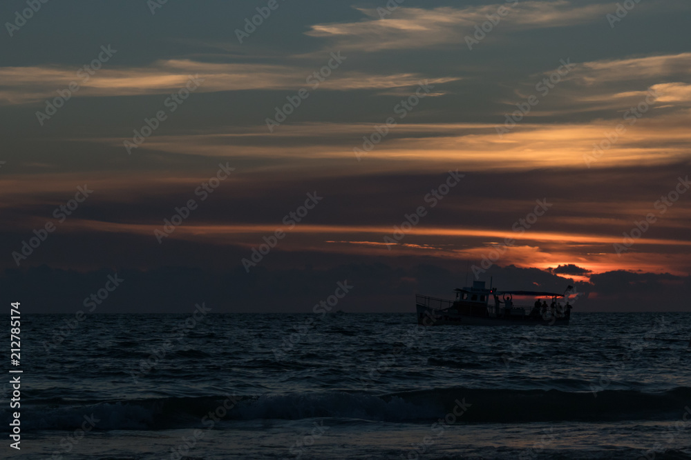 Silhouette of boat on the horizon at sunset on the beach