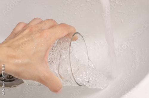Female hand water in a glass washbasin home drink
