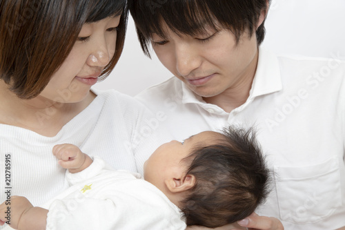 新生児を抱き見つめる若い夫婦、幸せな家族イメージ