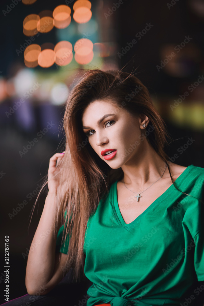Fototapeta premium Emotional portrait of Fashion stylish sexy of young hipster blonde woman, elegant lady, green top and red skirt, cool girl. City view urban dark cafe lifestyle background.
