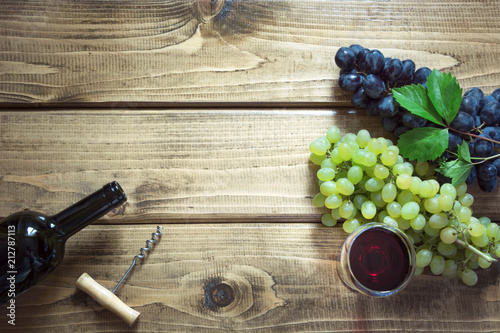 Open bottle of red wine with wineglass, corkscrew and ripe grape on wooden board. Copy space and top view.