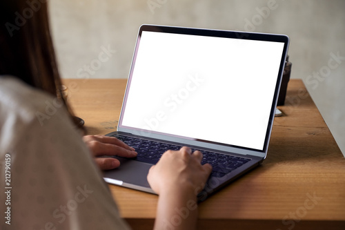 Mockup image of a woman using laptop with blank white desktop screen with coffee cup on wooden table