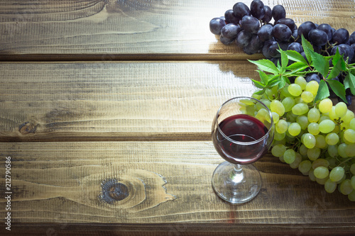 Wineglass with red wine and ripe grape on wooden board. Close up and copy space.