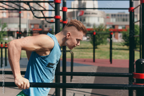 A young man on the Playground doing exercises on the bars