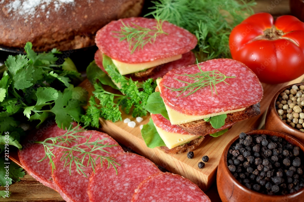 Sandwiches with salami, cheese and arugula salad surrounded by the ingredients