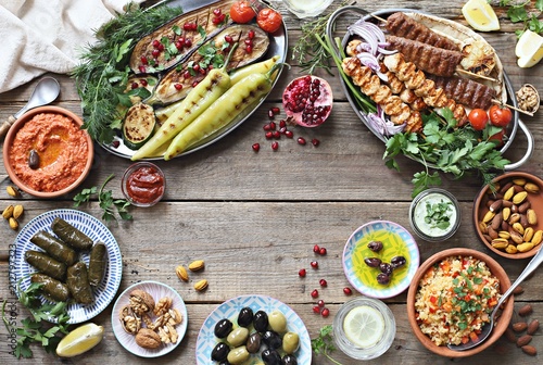 
    Middle eastern, arabic or mediterranean dinner table with grilled lamb kebab, chicken skewers with roasted vegetables and appetizers variety serving on wooden outdoor table. Overhead view. 
