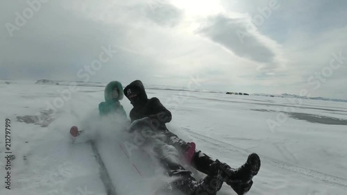 Children with their father ride on a plastic ice-boat tied to a car. This is extreme, dangerous and illegal. They are fun and funny. The snow flies in the face. Russian fun. photo
