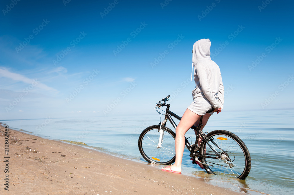 Fototapeta premium Young sporty lady resting from riding bicycle on the beach