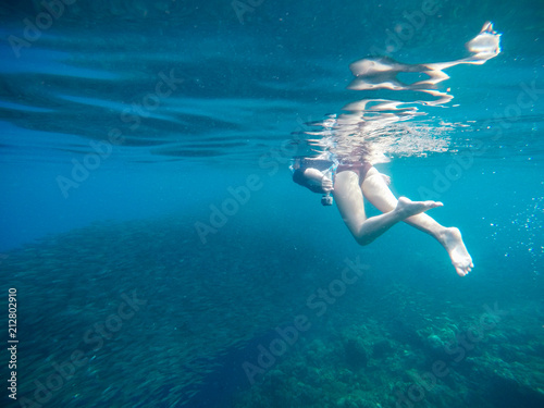 Woman swimming underwater in coral reef with sardine school. Summer vacation tourist with action camera.