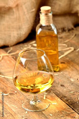 Glass of cognac on rustical wooden background and bottle in background vertical photo