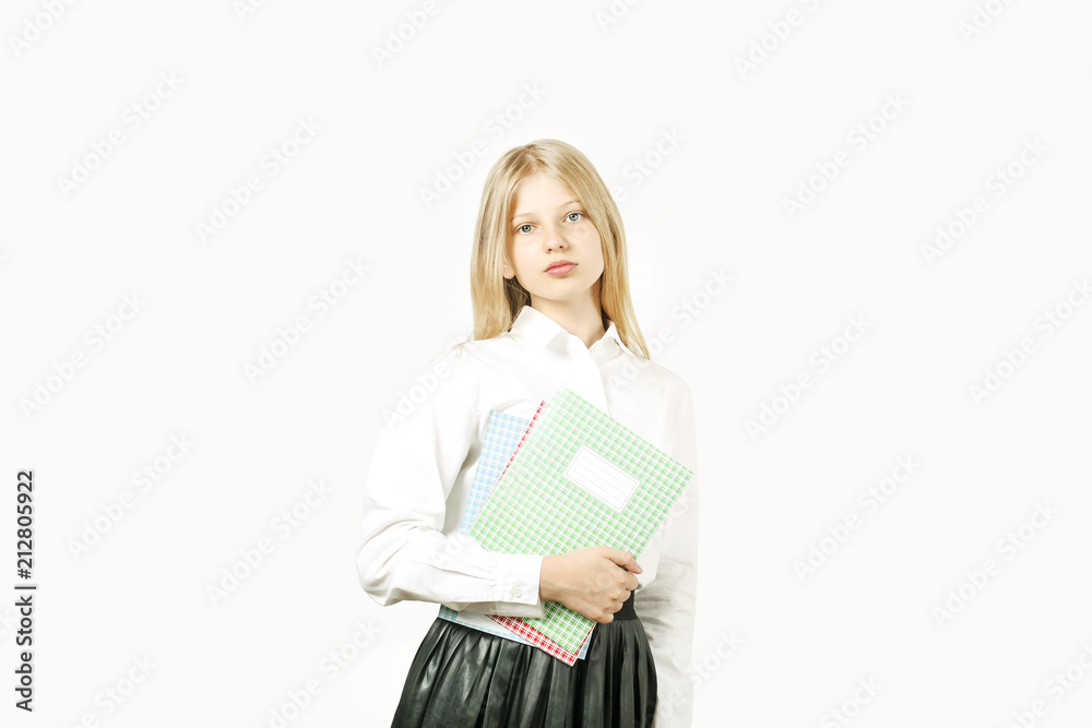 Beautiful blonde teenage girl with charming smile in schoolgirl uniform wearing pleated skirt, white shirt, holding notebooks. Back to school sale concept. Background, copy space, close up, isolated. Beautiful blonde teenage girl with charming smile in schoolgirl uniform wearing pleated skirt, white shirt, holding notebooks. Back to school sale concept. Background, copy space, close up, isolated.