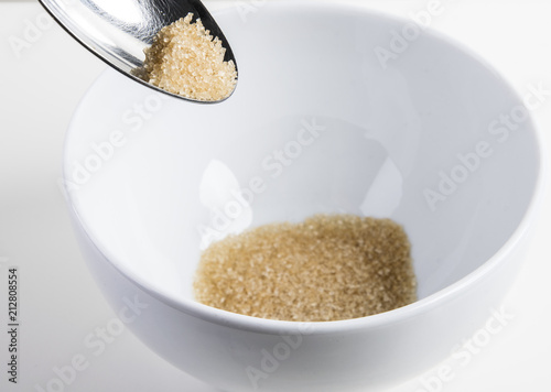 brown raw sugar on a silver spoon over a cerial bowl