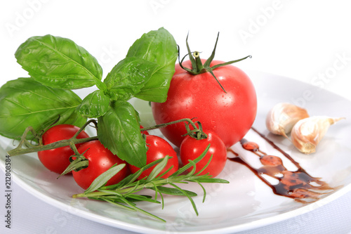 Pomidor czerwony, malinowy i koktajlowy, bazylia, rozmaryn i czosnek na talerzu.