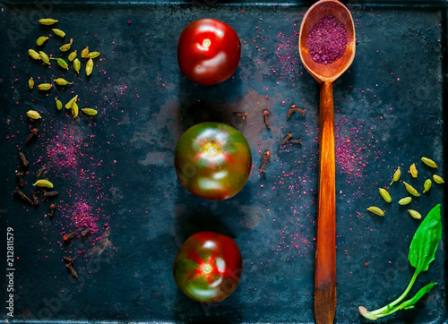 Black tomatoes cumato and wooden spoon with spice sumac .The concept of organic products and spices on vintage rusty metal background. Healthy food, vegan or diet nutrition concept, copy space