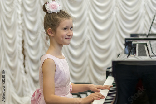 girl in a beautiful pink dress playing on a black grand piano. happy girl