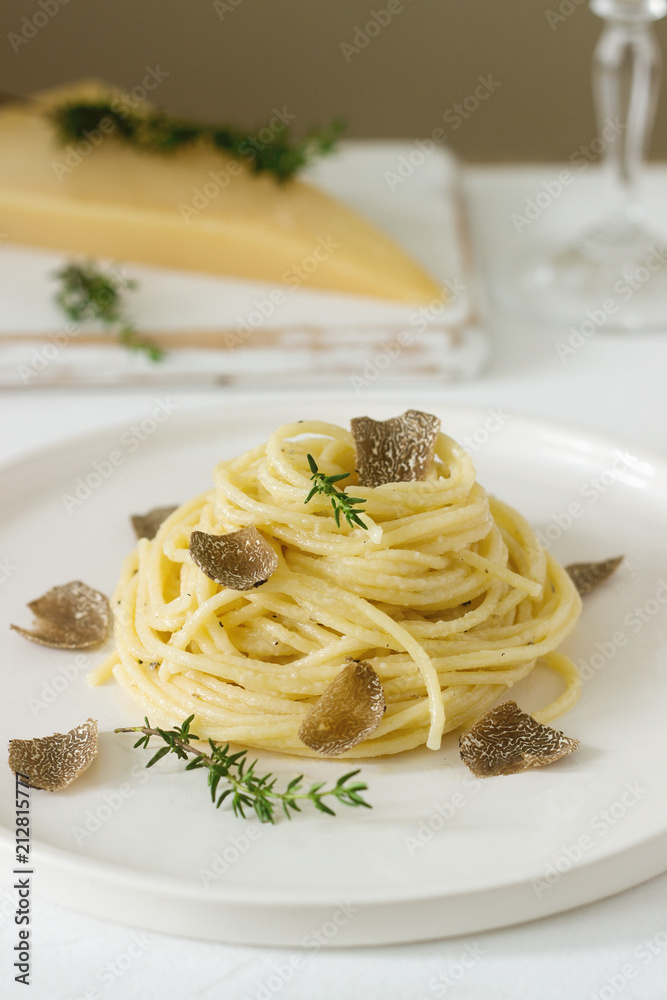 Pasta with creamy cheese sauce and truffle on a light plate, served with cheese and wine.