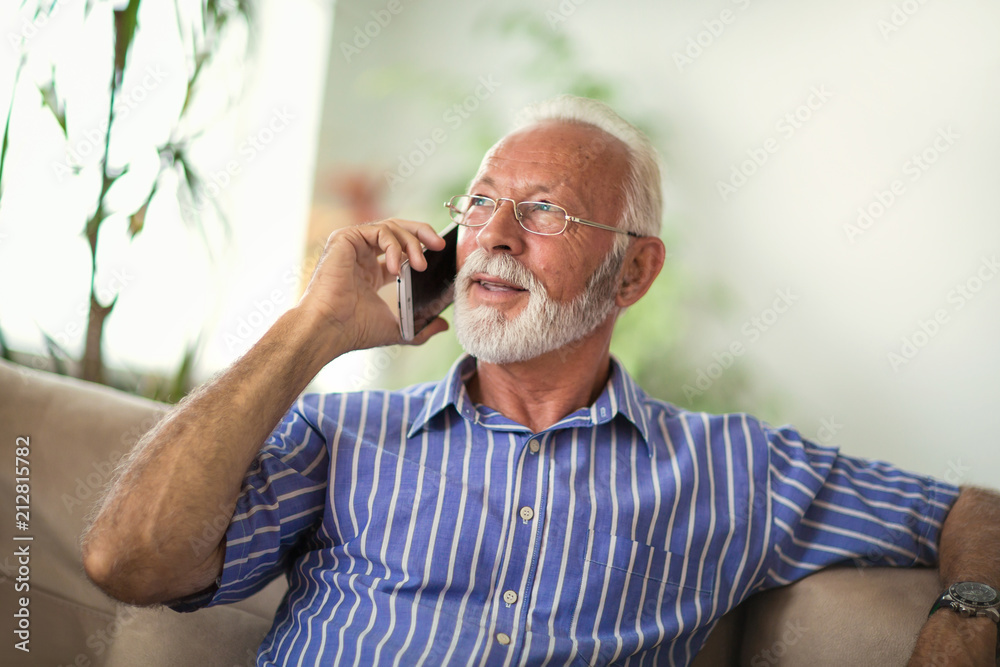 Senior man chatting on a mobile phone while relaxing on a sofa in his living room Senior man chatting on a mobile phone while relaxing on a sofa in his living room