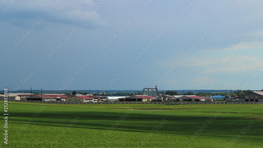 Beautiful rural landscape – green field in summer against the blue sky with clouds and farm on the horizon Beautiful rural landscape – green field in summer against the blue sky with clouds and farm on the horizon