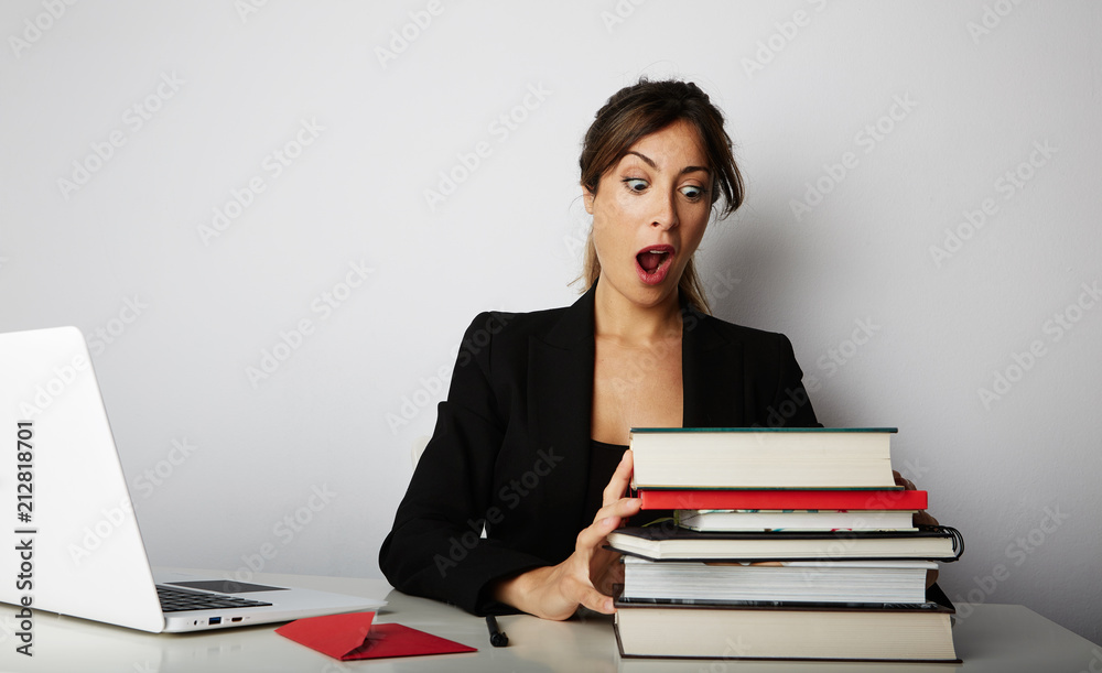 Young overwhelmed girl working hard. Young woman student shock of many books.Female model front of huge pile of books Young overwhelmed girl working hard. Young woman student shock of many books.Female model front of huge pile of books