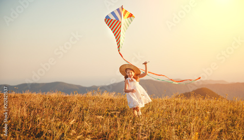 happy child girl running with kite at sunset outdoors