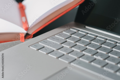 Closeup laptop keyboard and opened notebook with pen