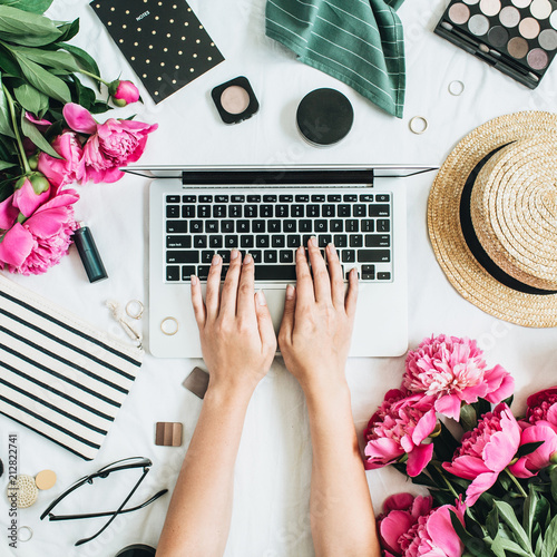 Flat lay styled office desk with laptop, pink peony flowers, cosmetics, accessories. Woman working on computer. Fashion or beauty blog background.