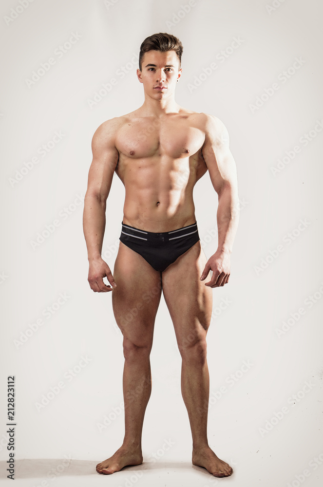 Handsome shirtless muscular man, standing, in studio shot, looking at camera, on white