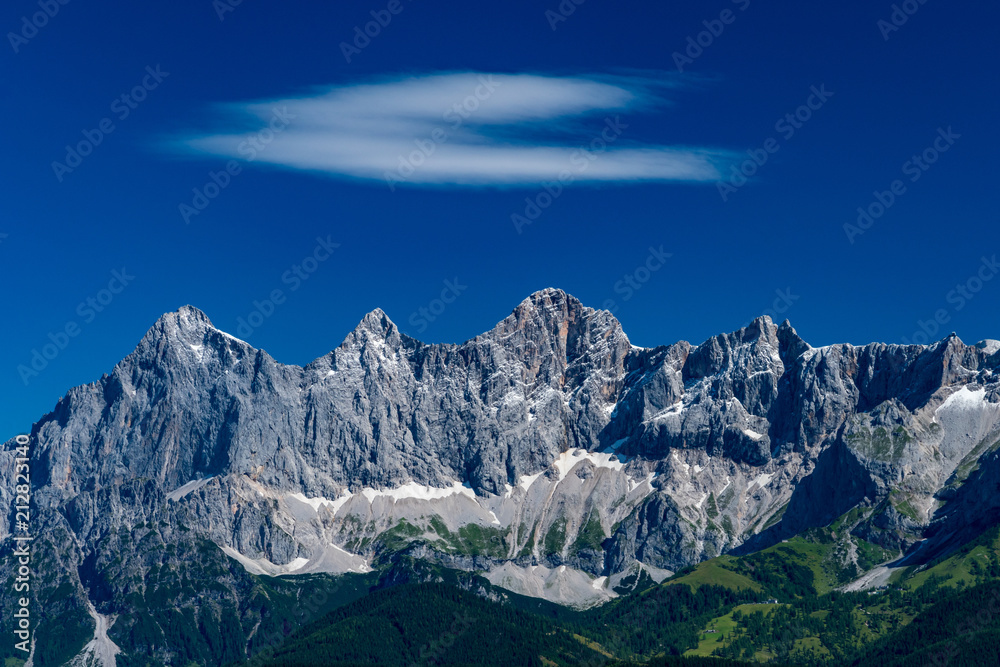 Hohe Dachstein mountain range in Austria with a soft white cloud on a deep blue sky
