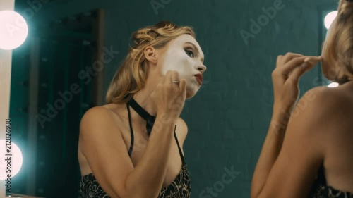 Young blond woman in dressing room doing stage makeup with white paint before performance