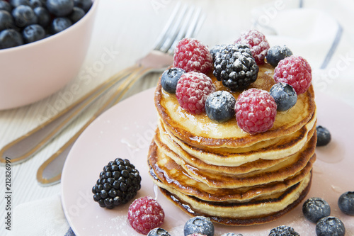 Stack of pancakes with raspberry, blackberry ,blueberry on white wooden background, side view. Close-up.