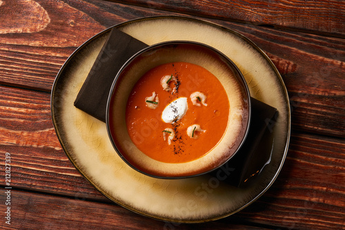 Tomato soup with shrimp. Seafood creamy soup with goat cheese, olive powder, wild shrimps on bowl plate at wooden table, top view, close-up. Delicious vegetarian diet food.