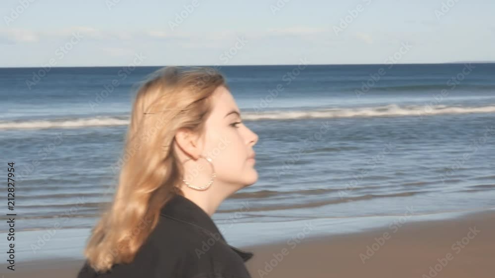 Attractive model girl walking along on beach thinking 4K slow motion Attractive model girl walking along on beach thinking 4K slow motion