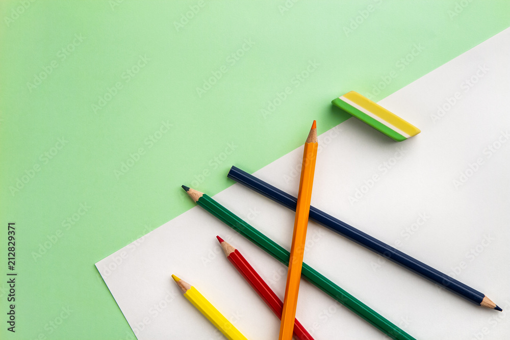 white sheet of paper, five pencils and an eraser on a light green paper background. Copy space white sheet of paper, five pencils and an eraser on a light green paper background. Copy space