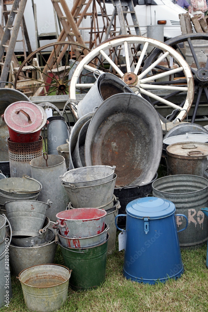 Group of old antique galvanied iron buckets and tin baths on display with various other vintage items including cart wheels Group of old antique galvanied iron buckets and tin baths on display with various other vintage items including cart wheels
