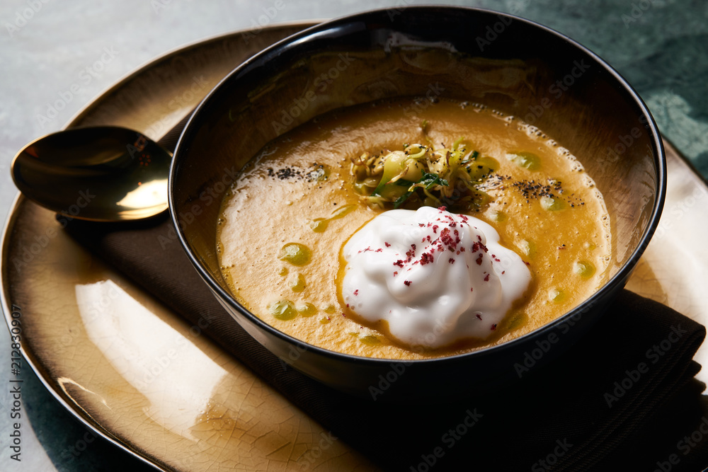 Pumpkin cream soup with cream and pumpkin seeds, coconut milk, green oil, sprouts of lentils in bowl plate on table, top view, close-up. Delicious vegetarian diet food 