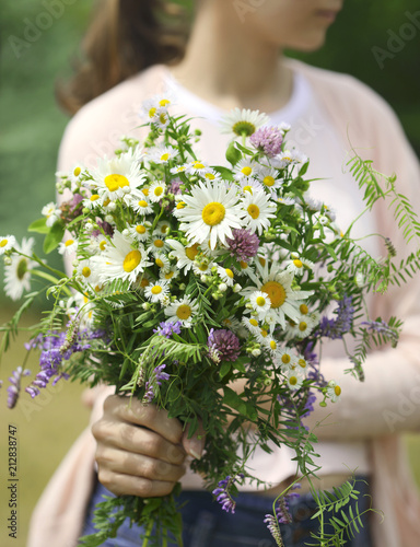 Fototapeta Naklejka Na Ścianę i Meble -  A young girl holding a bouquet of wildflowers in hands