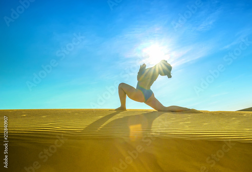 Silhouette woman performing yoga exercises workout on the sand dunes in the morning when the sun higher welcomes new day beautiful
