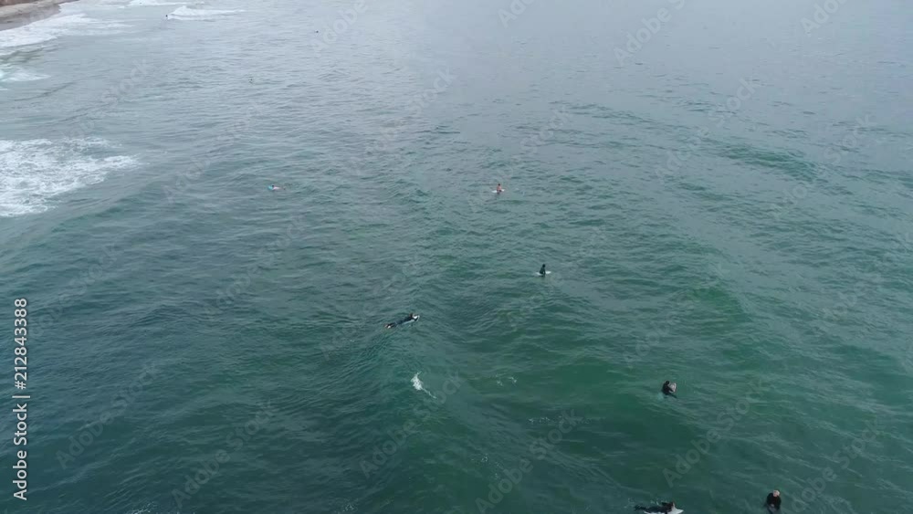 A pan down of several surfers waiting together for waves to catch